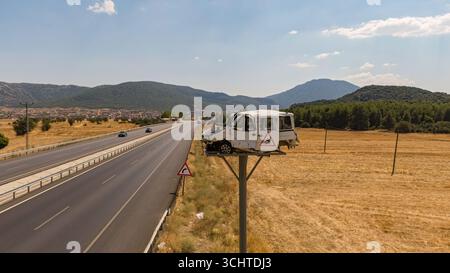 Ein abgestürztes Auto, das an einem Straßenpfosten montiert ist, als dramatische Verkehrswarnung auf einer Landstraße. Stockfoto