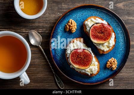 Zwei Sandwiches mit frischen Feigenscheiben, weißem Hüttenkäse, Honig und Walnüssen auf Toastbrot auf einem Teller, Blick von oben, Nahaufnahme. Gesunde Ernährung. Köstlich Stockfoto