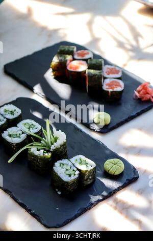 Sushi-Platten auf einem hellen Marmortisch. Eine Platte mit klassischen Gurken-Maki-Rollen, jede mit knuspriger Gurke und flauschigem weiß Stockfoto