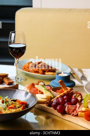 Elegantes Restaurant mit einem Glas Rotwein, einer Auswahl an Wurstwaren mit Käse, Trauben, Wurstwaren, Brotstangen und anderen Tapas Stockfoto