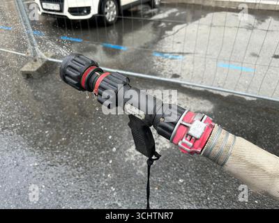 Ein Feuerwehrschlauch wird verwendet, um Wasser auf ein Auto zu sprühen. Der Schlauch ist an einen Hydranten angeschlossen und dient zum Waschen des Fahrzeugs Stockfoto