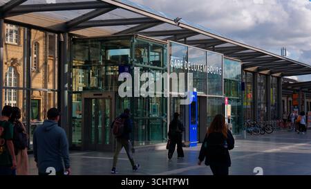 LUXEMBURG, EUROPA - 1. SEPTEMBER 2025 - Touristen, die in der Nähe des modernen Eingangs aus Glas und Stahl des Bahnhofs Gare de Luxembourg spazieren gehen Stockfoto