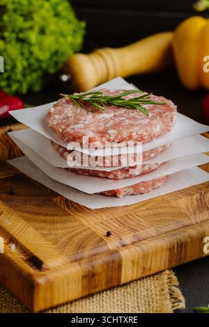 Stapel roher Burger-Patties mit Rosmarin auf Pergamentpapier, zum Grillen vorbereitet Stockfoto