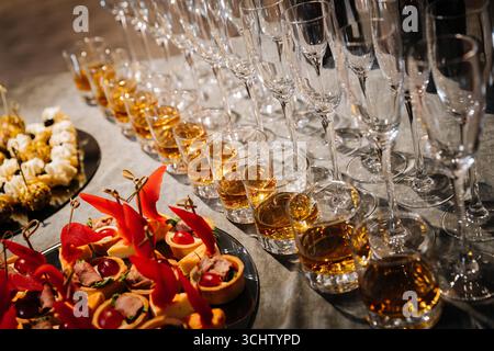 Elegantes Büfett mit Whiskey-Shots, Häppchen und Sektgläsern bei einer Luxusveranstaltung Stockfoto