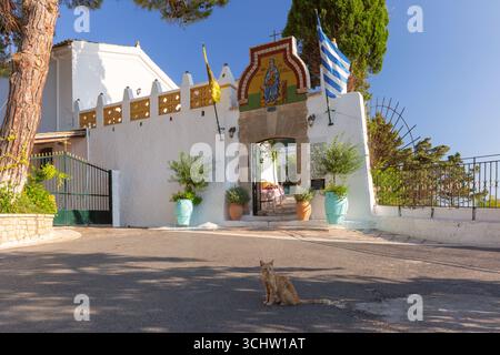 Eingangstor des Theotokos-Klosters in Paleokastritsa Korfu Griechenland mit griechischer Flagge und Katze auf der Straße Stockfoto