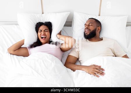 Unglücklich verzweifelt tausendjährige afroamerikanische Frau schreiend, bedeckt Ohren mit Kissen, leiden Schnarchen Stockfoto