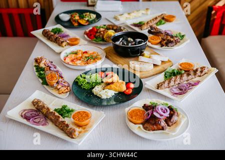 Gegrilltes Fleisch und Gemüse auf Tellern, serviert mit Saucen und frischen Kräutern Stockfoto