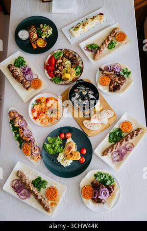Gegrilltes Fleisch und Gemüse auf Tellern, serviert mit Saucen und frischen Kräutern Stockfoto