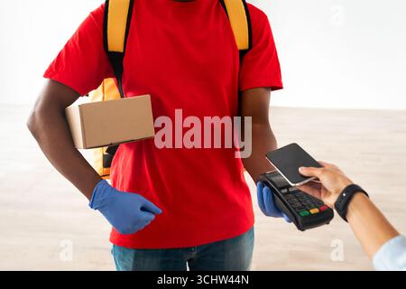 Schwarzer Mann mit POS-Maschine-Client, der mit Smartphone bezahlt Stockfoto
