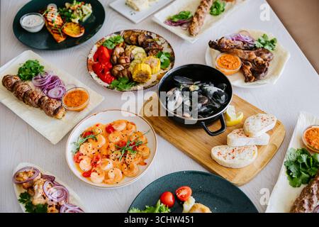 Blick von oben auf verschiedene gegrillte Fleischgerichte, Meeresfrüchte und Beilagen an einem Restauranttisch Stockfoto