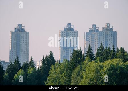 Drei hohe Wolkenkratzer dominieren die Skyline, die hoch über einem üppig grünen Wald stehen und einen eindrucksvollen Kontrast zwischen städtischer Entwicklung und natürlicher Schönheit schaffen Stockfoto