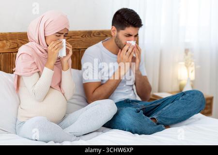 Das junge, schwanger-muslimische Paar bekam eine Grippe, hatte eine laufende Nase, saß zu Hause auf dem Bett und niesen in Papiergewebe Stockfoto