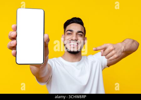 Glücklicher arabischer Kerl, der auf das Handy mit leerem Bildschirm zeigt Stockfoto