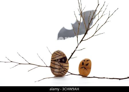 Zwei kreativ bemalte Steine, die Halloween-Charaktere darstellen, werden auf Ästen platziert, während eine Fledermaussilhouette einen Schatten im Hintergrund wirft, Addin Stockfoto