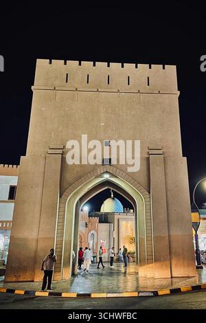 Besucher spazieren durch ein historisches Tor unter dramatischer Nachtbeleuchtung in Maskat City/19. Juli 2025, Maskat, Oman. Stockfoto