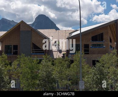 Zwei Bauarbeiter, die Kabelbäume verwenden, installieren Dachmaterialien in einem neuen Wohngebäude in Canmore, Alberta. Rundle Mountain bietet eine Kulisse. Stockfoto