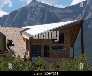 Zwei Bauarbeiter, die Kabelbäume verwenden, installieren Dachmaterialien in einem neuen Wohngebäude in Canmore, Alberta. Rundle Mountain bietet eine Kulisse. Stockfoto