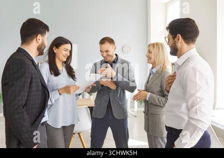 Eine Gruppe von Kollegen steht im Büro und lacht über einen lustigen Witz zusammen Stockfoto