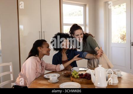 Verschiedene Freundinnen lachen und machen Selfie zu Hause mit Frühstück auf dem Tisch Stockfoto