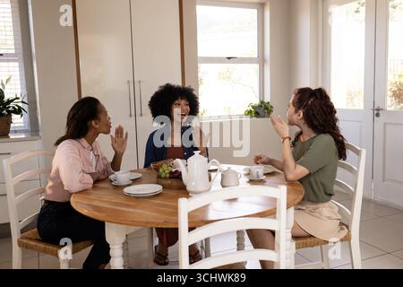 Verschiedene Freundinnen genießen morgens Tee und Unterhaltung zu Hause, lächeln und winken Stockfoto
