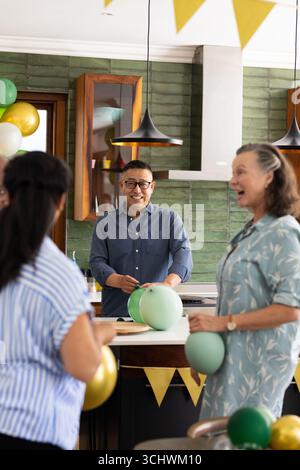 Verschiedene Seniorenfreunde genießen eine lebhafte Party, dekorieren mit bunten Ballons, Lachen, zu Hause Stockfoto