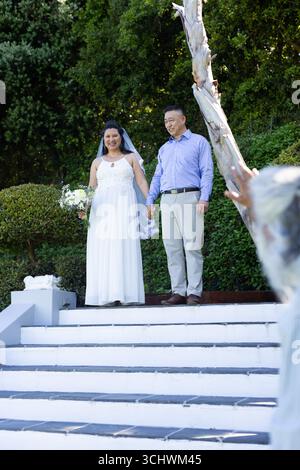 Ältere, vielfältige Paare stehen auf Gartentreppen, lächeln und halten Hände bei der Hochzeit Stockfoto