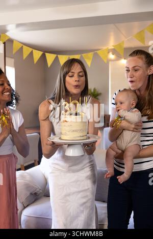 Verschiedene Freundinnen feiern Geburtstag mit Kuchen und Baby zu Hause und genießen freudige Momente Stockfoto