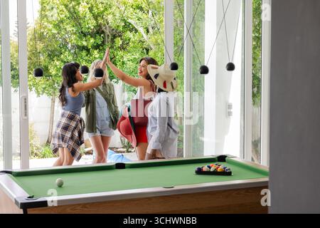 Frauen feiern mit High Fives in der Nähe des Billardtisches und genießen gemeinsame Freizeit Stockfoto