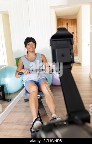 Frau, die zu Hause am Rudergerät trainiert, lächelt und fit bleibt Stockfoto