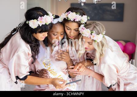 Auf dem Smartphone, Frauen in Blumenkronen, die aufgeregt die Brautschauer feiern Stockfoto