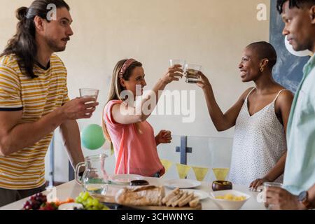 Freunde, die mit Gläsern tosten, genießen zwangloses Treffen mit Snacks und Getränken Stockfoto