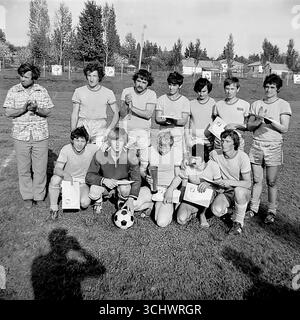 Eine Schwarzweißaufnahme aus dem Archiv, aufgenommen in Sviatohirsk in den 1970er Jahren Eine lokale Amateurmannschaft posiert für ein Gruppenfoto, nachdem sie ein Turnier gewonnen hat. Die Spieler und ihr Trainer stehen auf einem ländlichen Fußballfeld und halten ihre Auszeichnungen – Zertifikate und eine Trophäe. Das Foto vermittelt einen Geist der Kameradschaft und die Freude am Sieg, was die Kultur des Amateursports in der UdSSR widerspiegelt Stockfoto