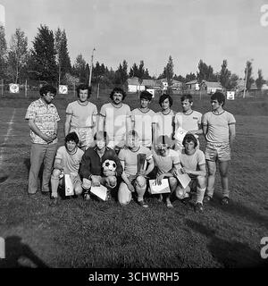 Eine Schwarzweißaufnahme aus dem Archiv, aufgenommen in Sviatohirsk in den 1970er Jahren Eine lokale Amateurmannschaft posiert für ein Gruppenfoto, nachdem sie ein Turnier gewonnen hat. Die Spieler und ihr Trainer stehen auf einem ländlichen Fußballfeld und halten ihre Auszeichnungen – Zertifikate und eine Trophäe. Das Foto vermittelt einen Geist der Kameradschaft und die Freude am Sieg, was die Kultur des Amateursports in der UdSSR widerspiegelt Stockfoto