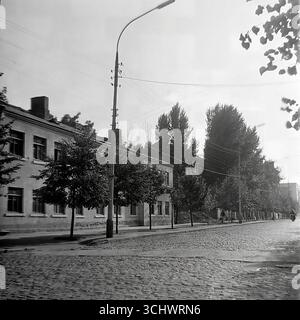 Eine Schwarzweißaufnahme aus dem Archiv, aufgenommen in Sloviansk in den 1960er Jahren Bankovska Straße, gepflastert mit Kopfsteinpflaster, während des Abrisses alter vorrevolutionärer Gebäude. Anstelle eines abgerissenen Hauses befindet sich ein leeres Grundstück und ein Haufen Bauschutt. Das Foto ist ein historisches Dokument, das die Rekonstruktion aus der Sowjetzeit und das sich verändernde historische Gesicht des Zentrums von Sloviansk feststellt Stockfoto