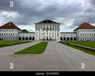 Vorderansicht des Schlosses Nymphenburg in München, Deutschland, unter dramatischen Wolken mit Menschen, die auf dem zentralen Pfad laufen. Stockfoto