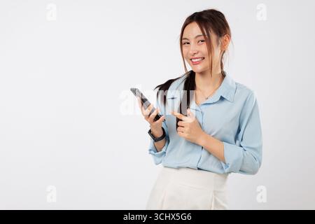 Glückliche asiatische Frau, die mit einer Hand auf das Telefon zeigt, während sie das Telefon selbstbewusst hält Stockfoto