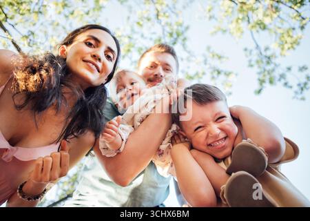 Gruppe von vier Familienmitgliedern, darunter zwei Kinder, lächelt und spielt zusammen im Freien, umgeben von üppigem Grün, zeigt Liebe und zusammen Stockfoto
