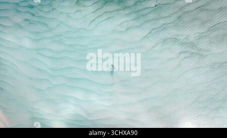 Aus der Vogelperspektive das türkisfarbene Wasser, das sanft um einen einsamen Paddleboarder plätschert, Moreton Island, Queensland, Australien. Stockfoto
