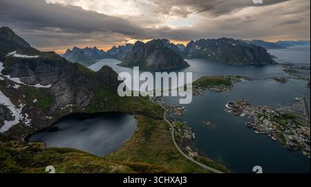 Aus der Vogelperspektive der dramatischen Fjorde treffen Sie auf das malerische Dorf, umgeben von zerklüfteten Gipfeln unter einem wilden Himmel, Srvgen, Nordland, Norwegen. Stockfoto