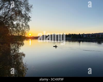 Sonnenuntergang über ruhigem Wasser mit einem Baum im Vordergrund Stockfoto