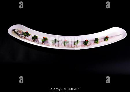 Ribbonfish (Trichiurus lepturus) Scheiben auf langer Porzellanplatte, schwarzer Hintergrund Stockfoto