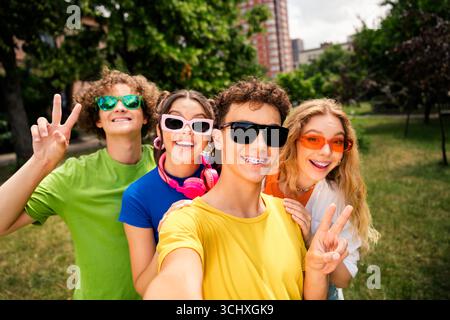 Gruppe glücklicher Teenager, die einen warmen Tag im Stadtpark genießen und Friedenszeichen und Lachen zeigen Stockfoto