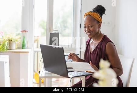 Lächelnde Frau mit Laptop, während sie am Schreibtisch im Büro sitzt Stockfoto