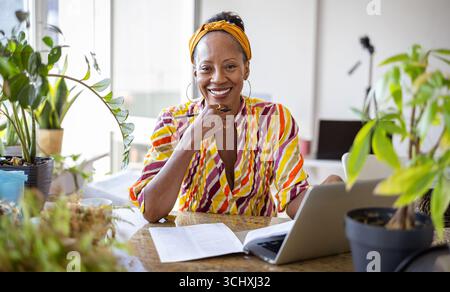 Lächelnde Frau mit Laptop, während sie am Schreibtisch im Büro sitzt Stockfoto