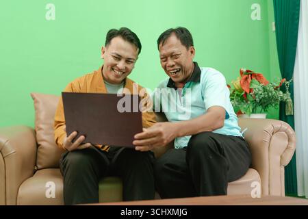 Zwei Männer, die freudige Momente zusammen auf einem Sofa genießen, während sie ein Notebook benutzen Stockfoto