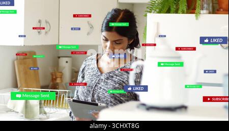 Überprüfen von Benachrichtigungen in sozialen Medien Frau, die ein Tablet in der Küche hält, mit Geschirr- und Topffarn Stockfoto
