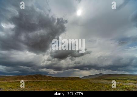 Blick auf einen dramatischen Himmel voller dunkler, wirbelnder Wolken, die über einer weiten, offenen Landschaft hängen und Schatten auf die sanften Hügel werfen, Deosai National Pa Stockfoto
