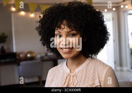 Lächelnde Frau mit lockigem Haar, die zu Hause festliche Feierlichkeiten genießt Stockfoto