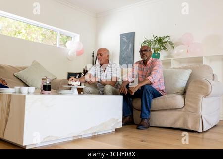 Ältere Freunde genießen Kaffee und Kuchen zusammen in gemütlicher Wohnzimmeratmosphäre Stockfoto