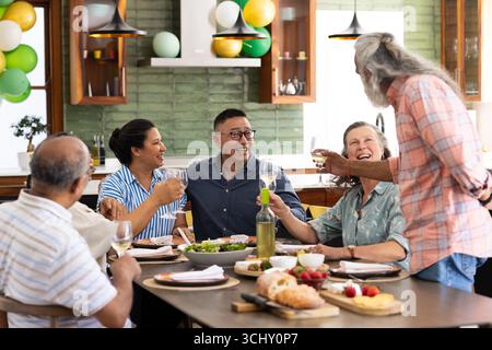 Verschiedene Seniorenfreunde, die zu Hause eine Dinnerparty genießen, lachen und mit Wein rösten Stockfoto